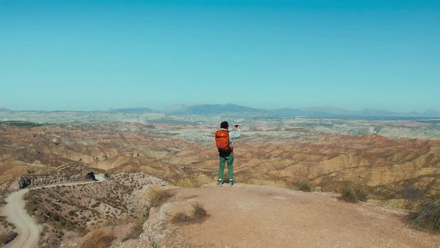 Male adventurer at the top of a hill, making photo with phone of the majestic mountains. Wanderlust-filled journey offers a peaceful escape from everyday life. Travel blog concept. 