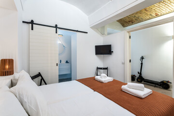 Fototapeta na wymiar Traditional modern Iberian bedroom with brick ceiling and clean towels and linens. in the corridor electric scooter