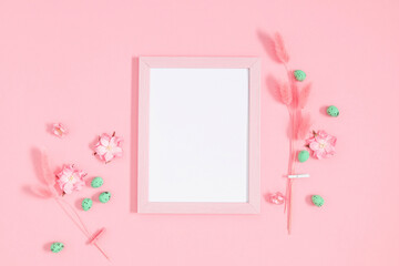 Easter decor, composition. Empty photo frame, flowers, easter eggs on pastel pink background. Flat...