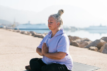 Fototapeta na wymiar Senior woman with dreadlocks in stretching position by the sea at morning. Elderly woman doing yoga near beach.