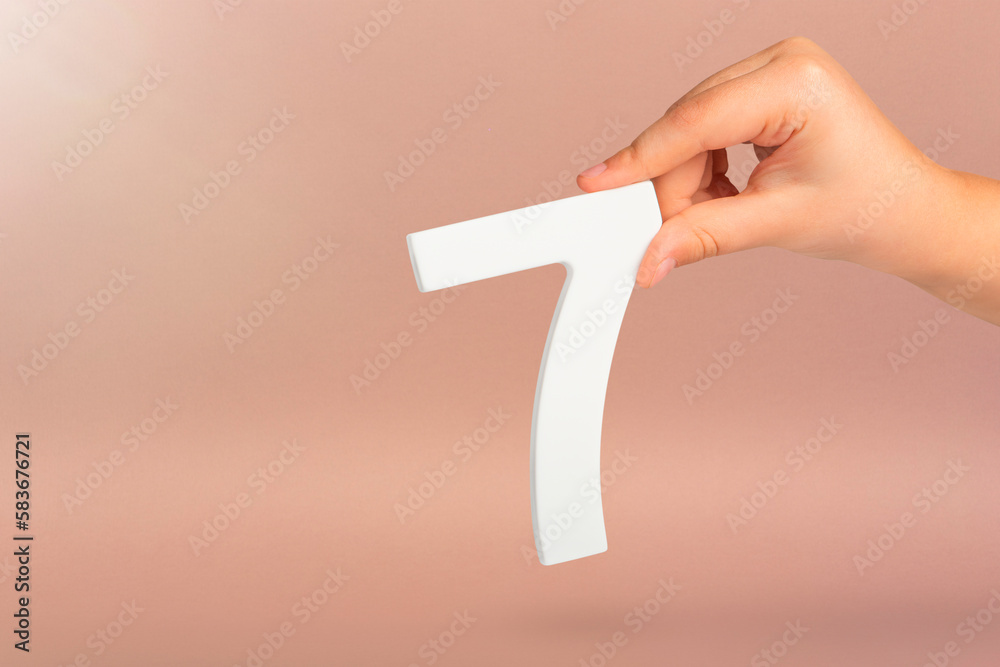 Aufkleber number seven in hand. hand holding white number 7 on red background with copy space. concept with nu