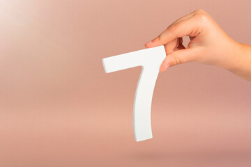 Number seven in hand. Hand holding white number 7 on red background with copy space. Concept with...