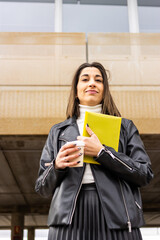 Portrait of smiling female entrepreneur in formal suit with yellow folder and coffee outdoors. Young smart casual clothing businesswoman portrait