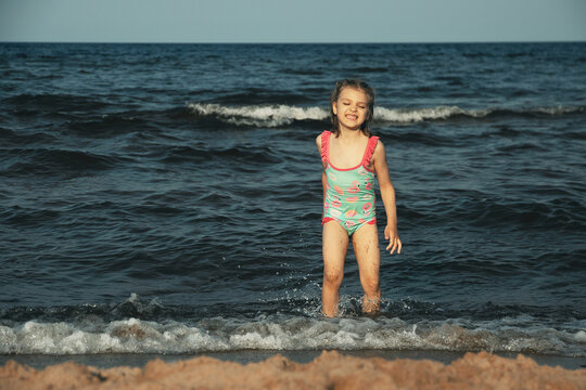 laughing girl of 5 years in blue swimsuit runs in sea water