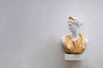 Antique head bust of woman against gray wall. Historical statue in golden dress himation. Ancient...