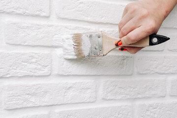 A woman paints a brick wall with white paint. She holds a brush in her hand. Painting tiles DIY