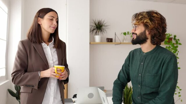 Two young business people talking in the office. Businesswoman having a coffee break with male colleague at workplace. Teamwork and business concept