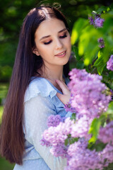 Happy girl with long hair stands with lilac flowers, in the garden