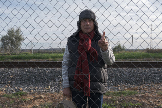 senior man with red scarf behind a fence near the train tracks