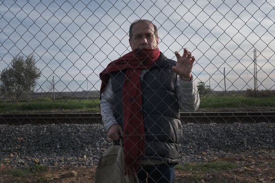 senior man with red scarf behind a fence near the train tracks