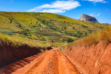 Fototapeta na wymiar Red dust and mud road in poor condition with ridges formed after rain. Routes to Andringitra national park are bad during wet season in region near Ambalavao, Madagascar