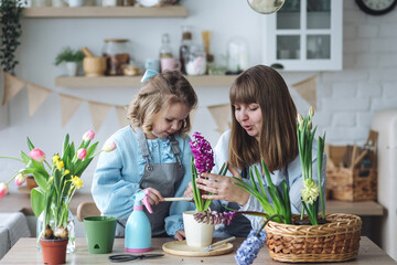 Obraz na płótnie Canvas Happy mother and daughter doing home gardening together in the kitchen, taking care about flowers, plants. Family traditions and quality time, having fun, enjoy domestic life. Mother's or Women's day