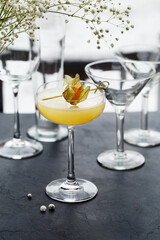 Yellow cocktail in glass decorated with physalis over dark concrete background. Side view, close up