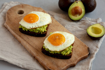 Homemade Avocado Toast with Eggs on a rustic wooden board, side view.