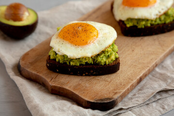 Homemade Avocado Toast with Eggs on a rustic wooden board, side view.