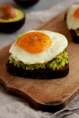 Homemade Avocado Toast with Eggs on a rustic wooden board, side view. Close-up.