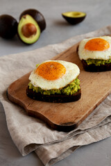 Homemade Avocado Toast with Eggs on a rustic wooden board, side view.