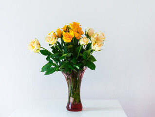 Yellow roses in a glass vase on light soft background in minimalist style home interior. 