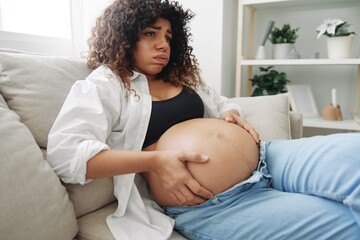 Pregnant woman headache lies at home in a shirt and jeans on the couch fatigue and heaviness in the last month of pregnancy before childbirth, lifestyle difficulties of motherhood, nausea