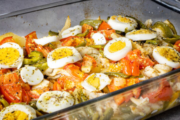Gomes de sa codfish roasted in olive oil with tomatoes, peppers, onions, boiled eggs and oregano. In a rectangular glass baking dish.