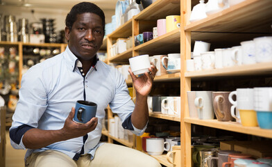 Focused african american man visiting household goods store in search of dishware, looking for new...