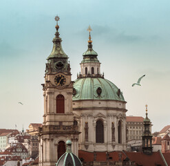 Fototapeta na wymiar Cityscape of Prague with St Nicholas Church and Bell Tower with Clock in Lesser Town. Religious architecture in Baroque style, old buildings and city landmark in historic downtown of Praga.