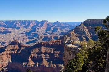 Bright desert sunlight shines down on the Grand Canyon, casting shadows on every crease and layer of the eroded canyon carved over many years by the Colorado River thousands of feet below