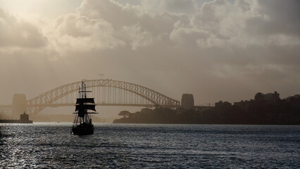 Silhouetted schooner barque tall ship sailing towards Harbour Bridge in a hazy afternoon....