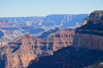 Bright desert sunlight shines down on the Grand Canyon, casting shadows on every crease and layer of the eroded canyon carved over many years by the Colorado River thousands of feet below