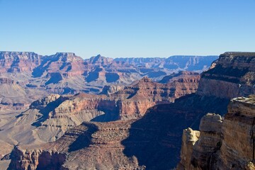 Bright desert sunlight shines down on the Grand Canyon, casting shadows on every crease and layer of the eroded canyon carved over many years by the Colorado River thousands of feet below