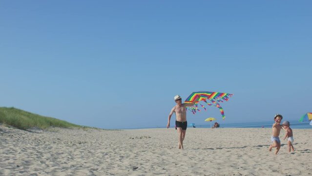 happy family on summer beach father and his sons fly colorful kite blue sky. man and two little boys running white sand laughing looking kite in hands waiting wind. sea ocean seaside summer vacations