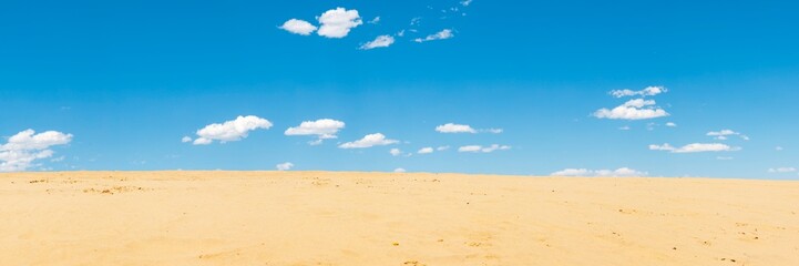 Fototapeta na wymiar Sand dunes and blue sky with white clouds, natural background.