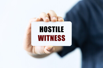 Hostile witness text on blank business card being held by a woman's hand with blurred background. Business concept and legal concept about hostile witness.
