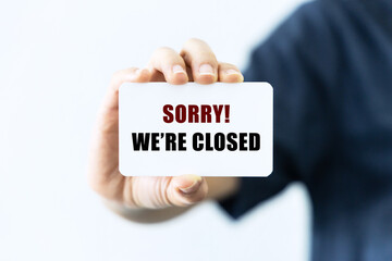 Sorry we are closed text on blank business card being held by a woman's hand with blurred background. Business concept to inform audience that we are closed.