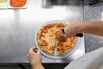 Chef cutting freshly baked pizza with round knife on wooden board