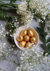 Foil wrapped Easter chocolate eggs in a glass bowl. Easter celebration concept. Colorful still life with sweets. Textured background with copy space. Easter greeting card. 