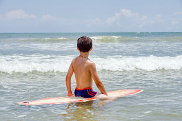 Young preteen boy surfer sitting in the water on his surfboard while watching for waves