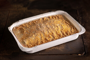 Frozen lasagna in paper form on a dark background. Semifinished.