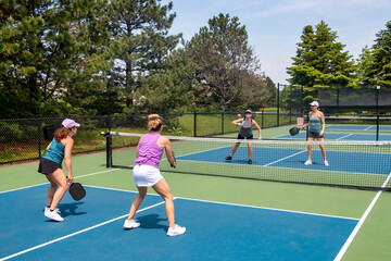Two players approach the net in a competitive doubles game of pickleball on a blue and green court in summer.