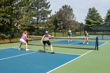 Two players approach the net in a competitive doubles game of pickleball on a blue and green court in summer.