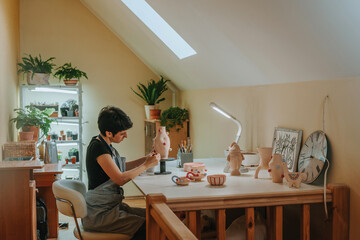 Young woman potter painting a vase at workshop