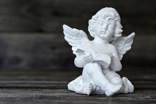 Guardian angel reading a book. Angel figurine on wooden background with copy space.