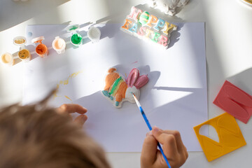 A child paints an Easter bunny figurine. Easter children's crafts.