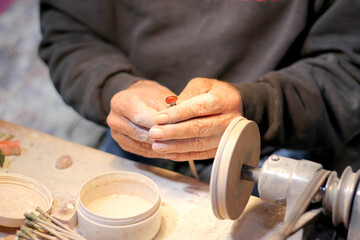 Hands of elderly craftsman man working in a workshop polishing opal stones and minerals to form precious jewelry
