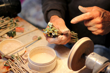 Hands of elderly craftsman man working in a workshop polishing opal stones and minerals to form precious jewelry
