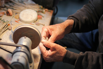 Hands of elderly craftsman man working in a workshop polishing opal stones and minerals to form precious jewelry
