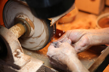 Hands of elderly craftsman man working in a workshop polishing opal stones and minerals to form precious jewelry
