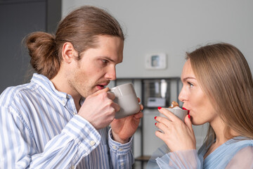 Two young people with beautiful long hair in light blue clothes are drinking coffe. The eyes of a man and a woman  talking. They enjoy each other`s attention. The shelf is in the background. Copyspace