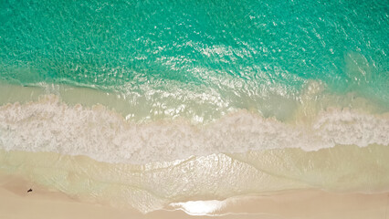 Aerial top view of ocean blue waves break on a beach. Sea waves and beautiful sand beach aerial view shot. Tropical beach with turquoise ocean water and waves, aerial view. Top view of paradise island