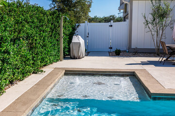 The hot tub spa tanning ledge portion of a new swimming pool with tan concrete edges in the fenced...